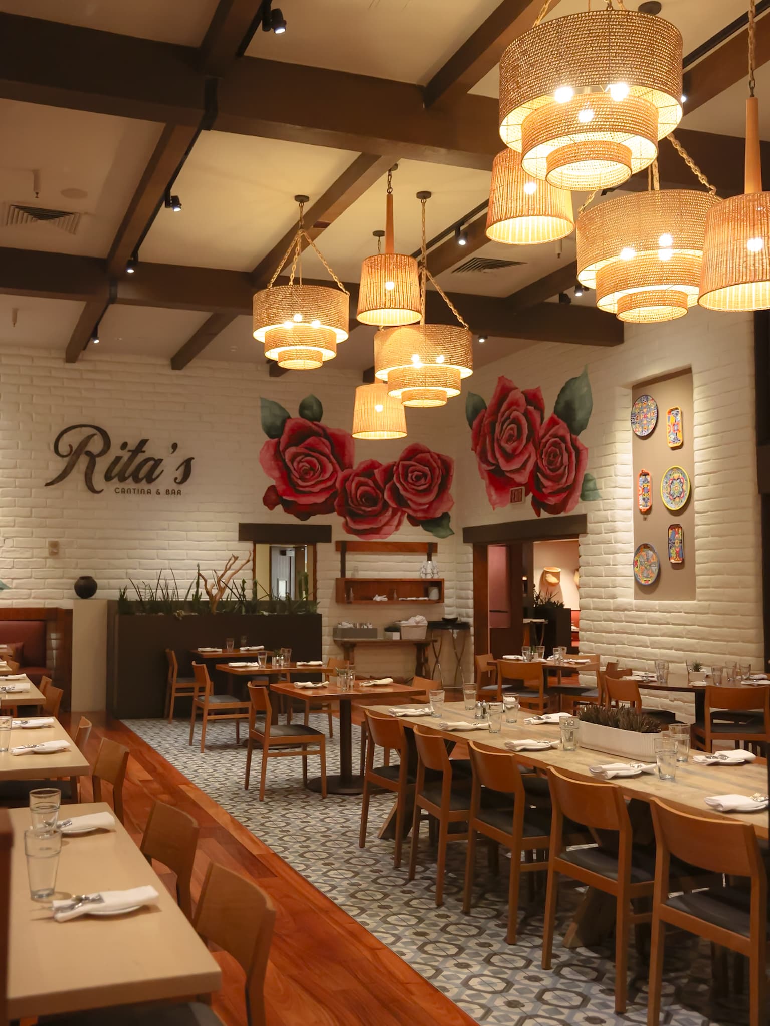 Warm interior dining room at Rita’s Cantina & Bar inside JW Marriott Scottsdale Camelback Inn with woven chandeliers, floral wall murals, and set tables.