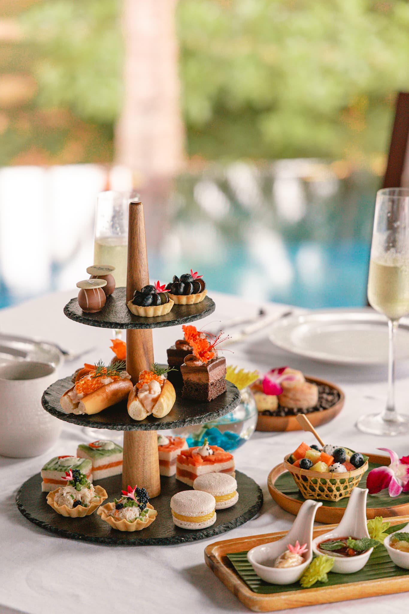 Luxury afternoon tea presentation at Ritz-Carlton Phulay Bay Reserve with pastries, fruit, champagne, and poolside tropical views.