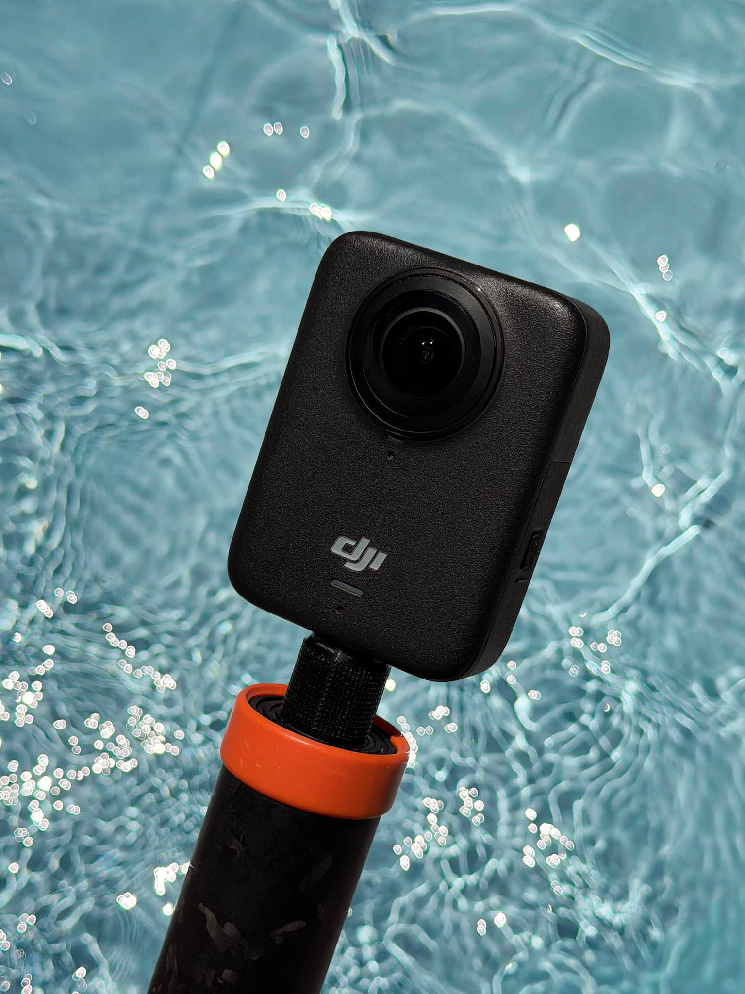 Close-up of a DJI Osmo 360 action camera mounted on a handle above sparkling blue pool water.