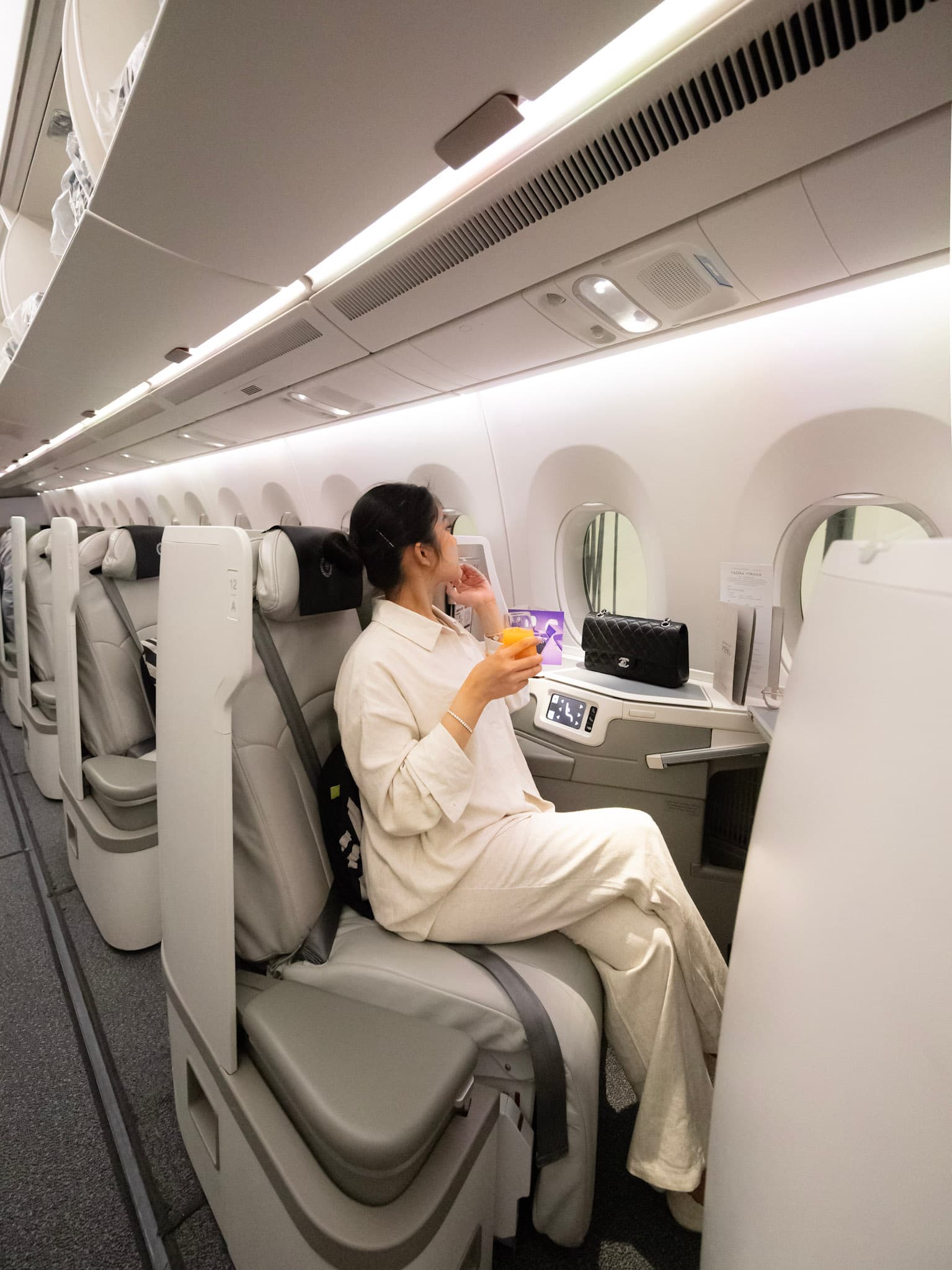 Tram Le seated in a Fiji Airways business class cabin holding a drink and looking out the airplane window during a travel collaboration.