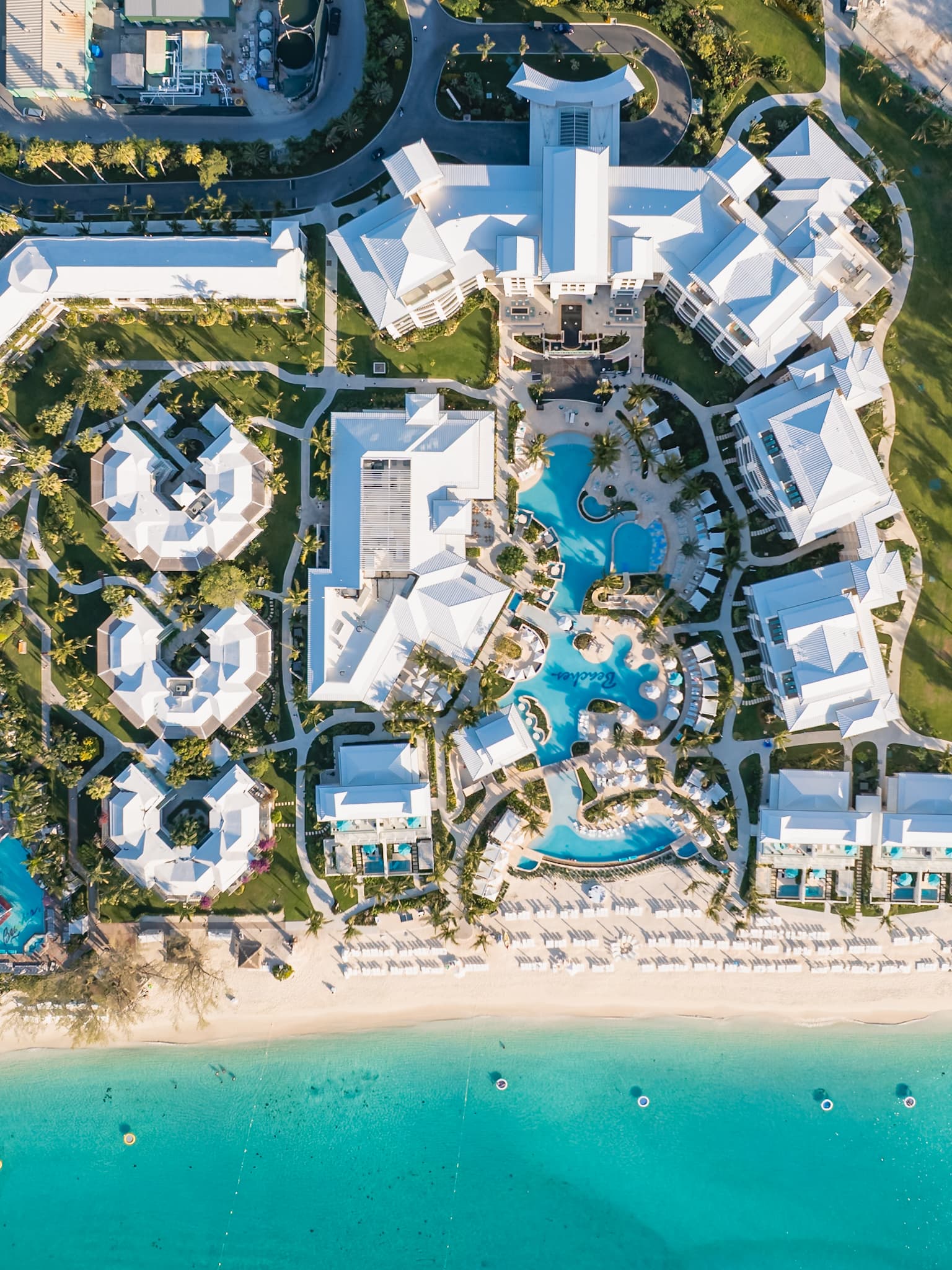 Aerial view of Beaches Resort with beachfront pools, white resort buildings, palm trees, and turquoise ocean water.