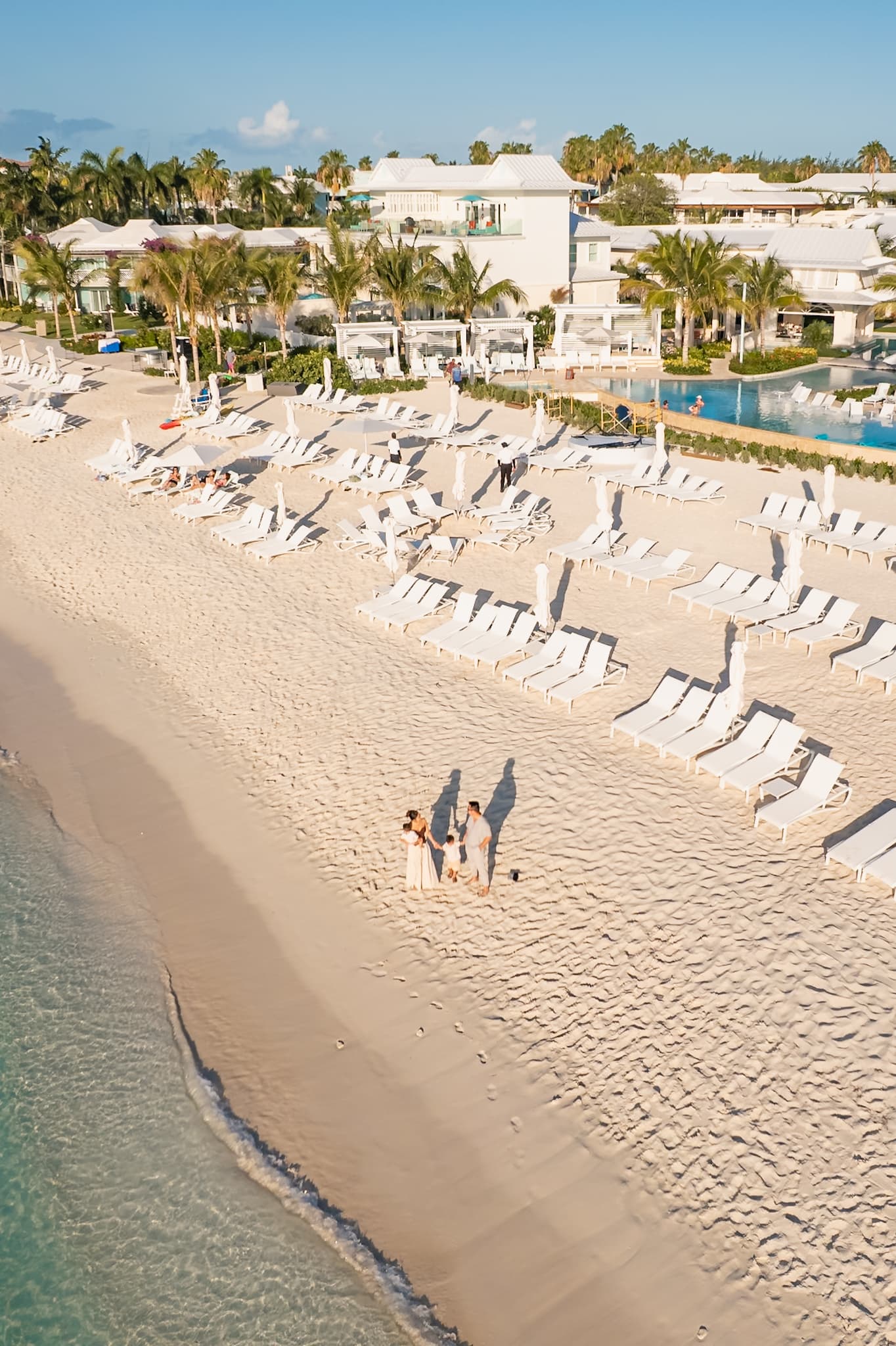 Aerial view of a family standing on the white sand beach at Beaches Resort with lounge chairs, palm trees, pools, and turquoise ocean water.