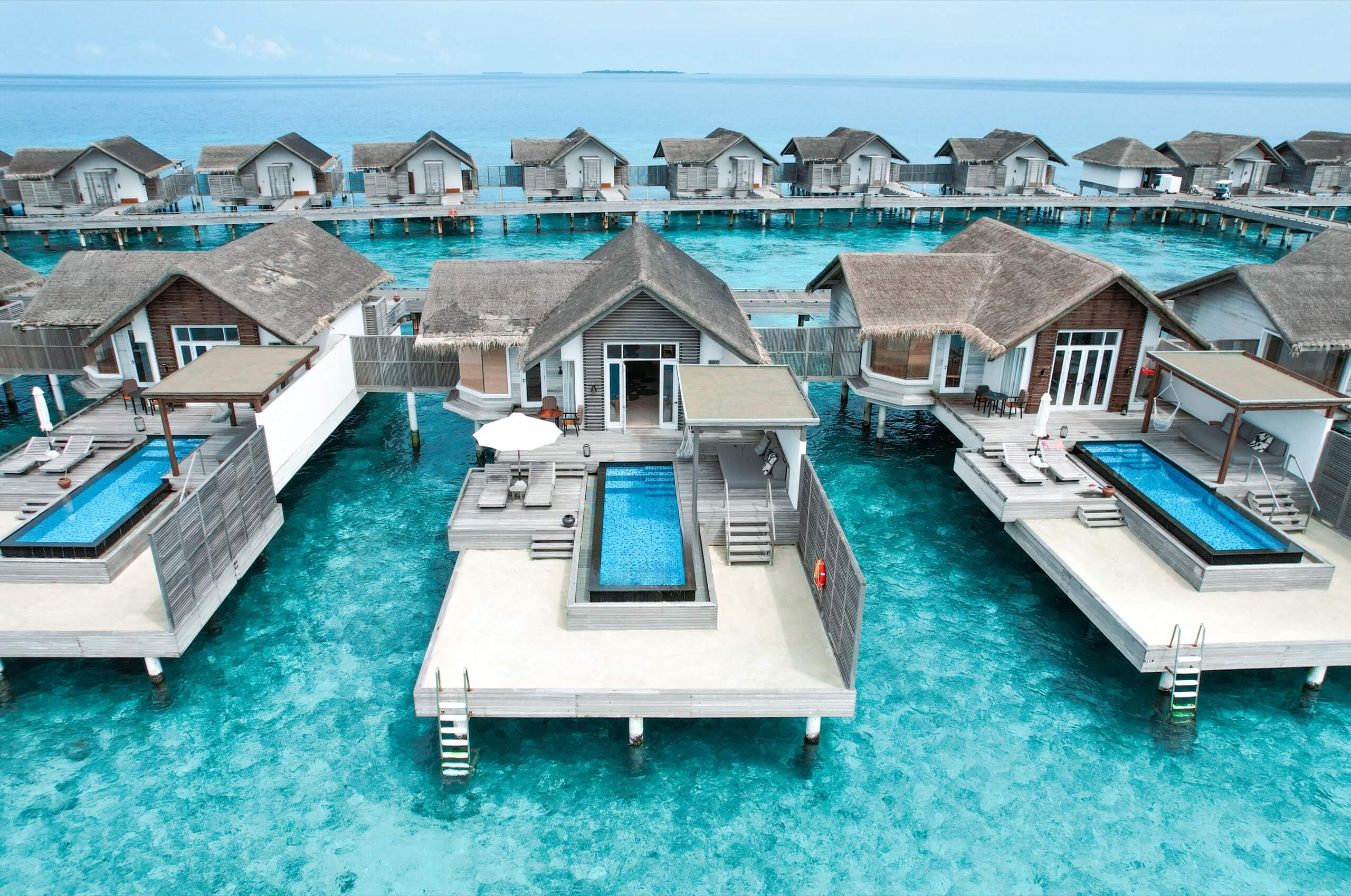 Overwater villas with private pools at Fairmont Maldives surrounded by clear turquoise lagoon water.