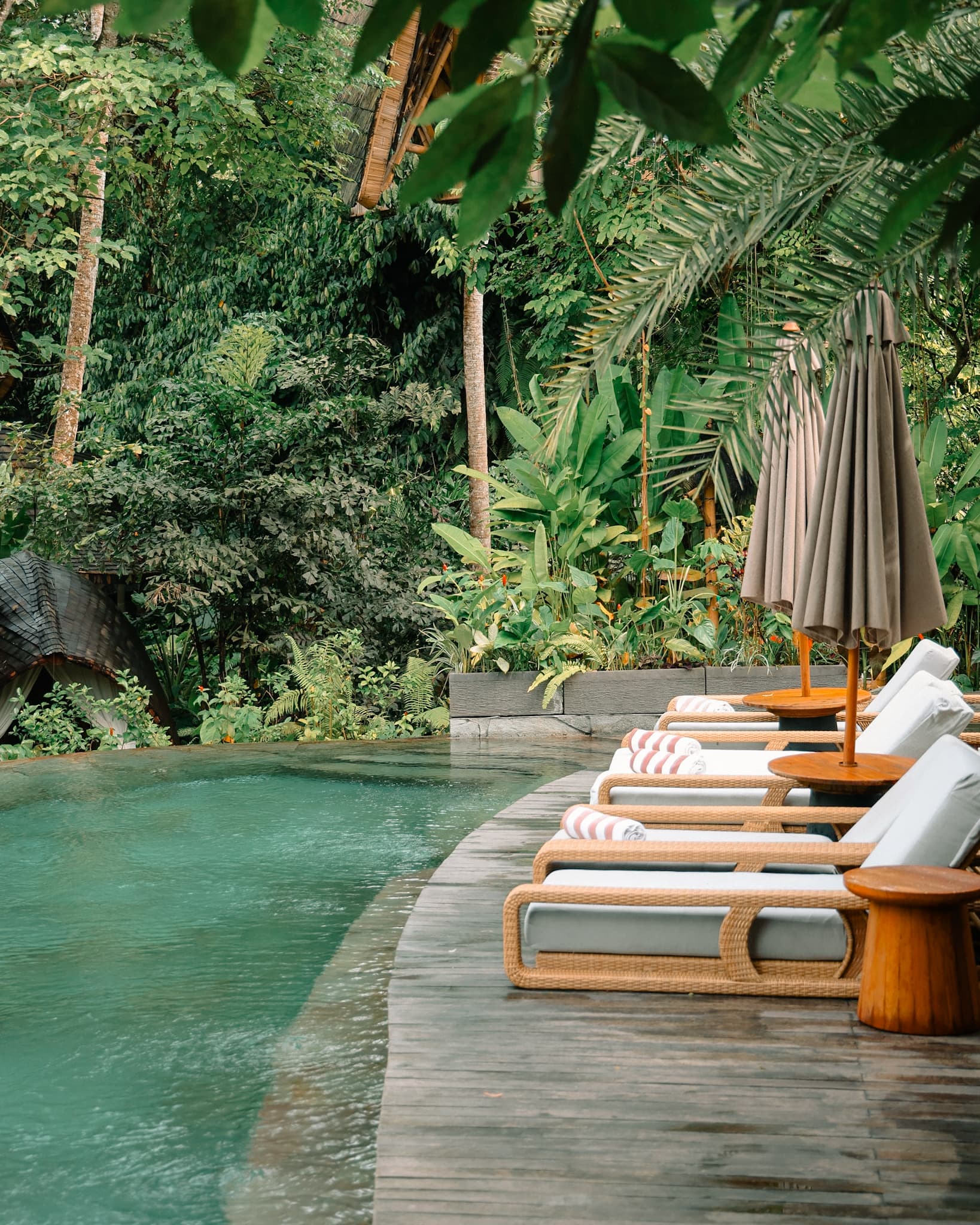 Poolside lounge chairs beside a jungle swimming pool surrounded by tropical greenery at Ulaman Resort in Bali.